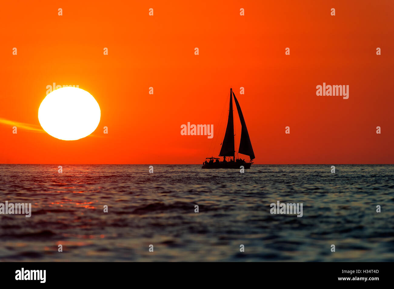 Coucher du soleil est un voilier avec équipage à bord du bateau qui se profile la voile le long de l'océan de l'eau avec un bain de soleil blanc dans le soleil rouge Banque D'Images
