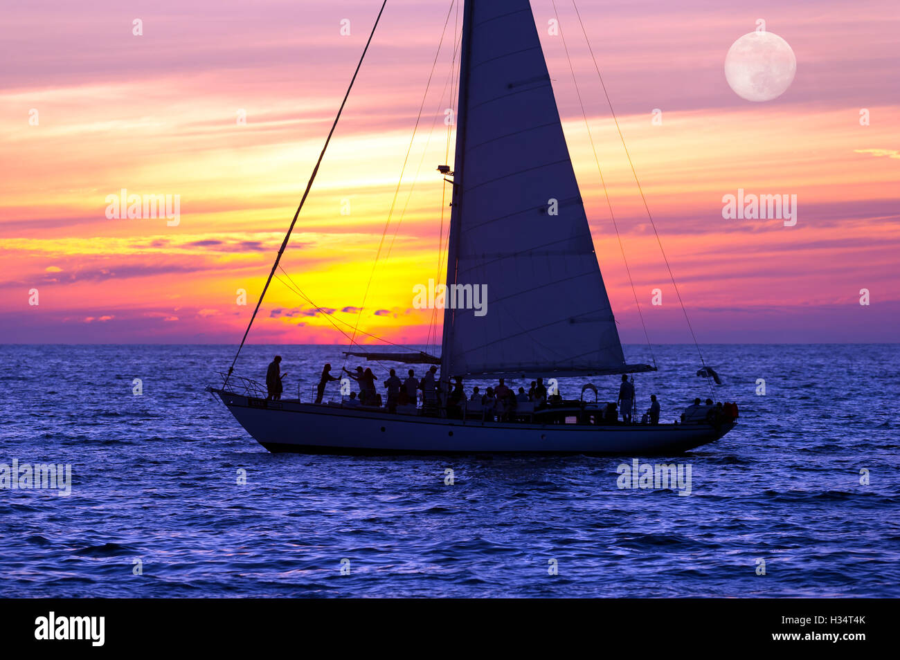 Voilier coucher du soleil est un bateau plein de gens naviguant le long de l'océan de l'eau avec un coucher de soleil dans l'arrière-plan. Banque D'Images