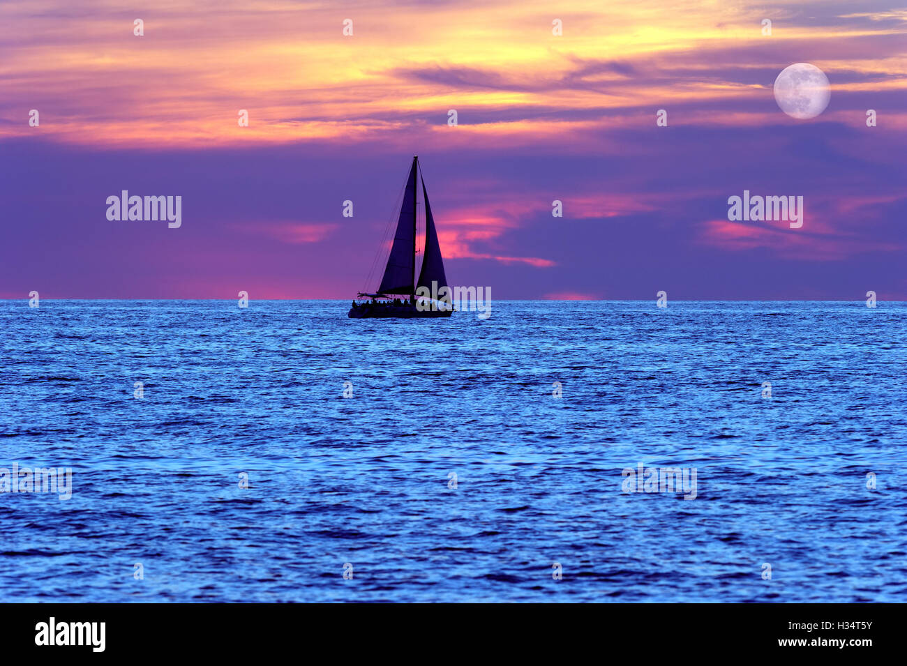 Voilier coucher de lune est une silhouette d'un bateau naviguant au bord de l'eau avec toutes voiles dehors en tant que la lune se lève dans le ciel du soir Banque D'Images