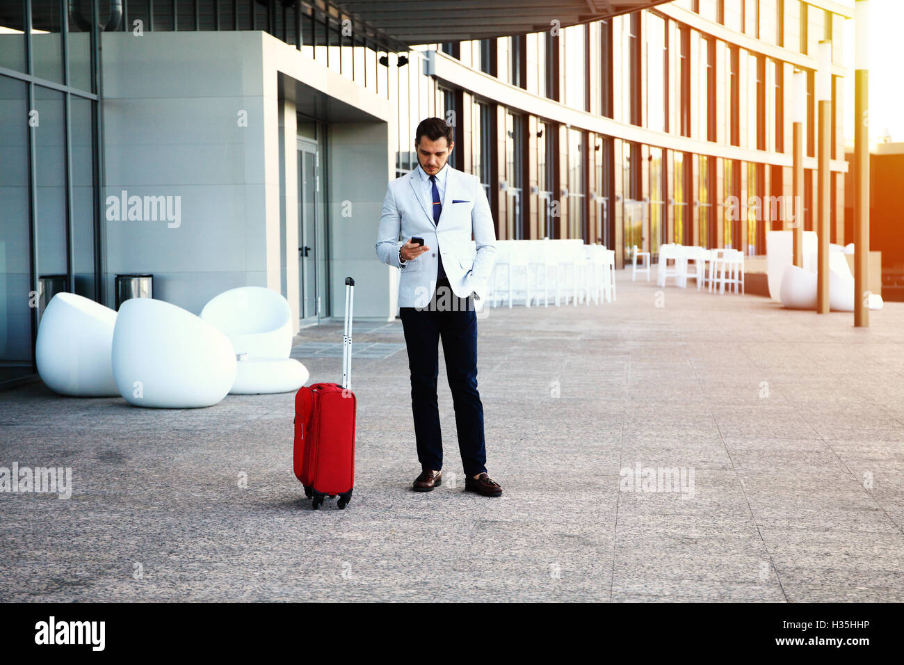 Young happy traveler businessman making appel après son arrivée à l'extérieur de l'hôtel avec ses bagages. Banque D'Images