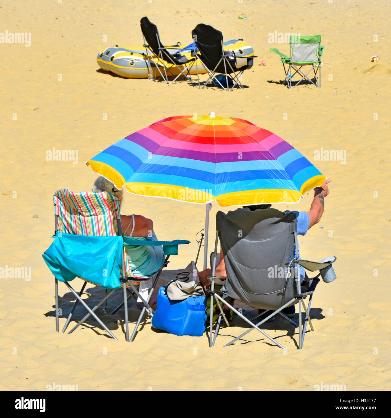 D'âge mûr sous UK parasol coloré en relaxant pli jusqu'à des chaises sur la plage de sable de mer maison de vacances à l'ombre du chaud soleil d'été Banque D'Images