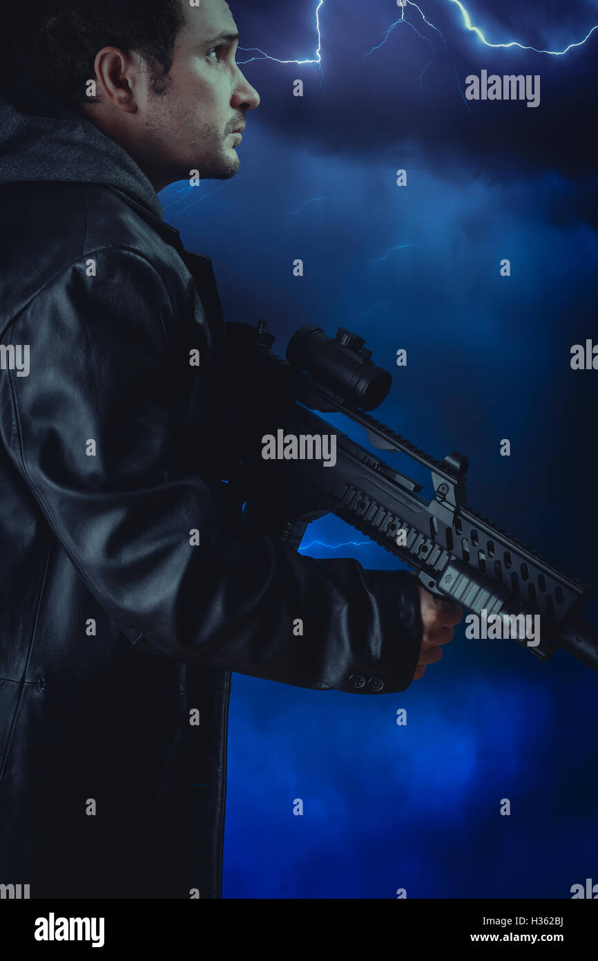 Veste en cuir longue homme avec un fusil d'assaut et sur fond de tempête Banque D'Images