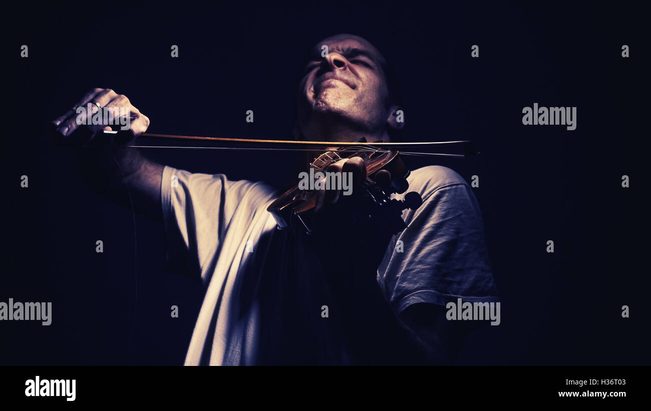 Homme adulte joue un violon, dans une ambiance sombre, montrant les émotions et les expressions. Banque D'Images