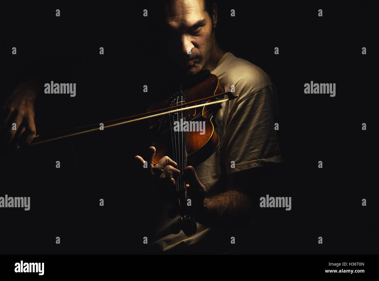 Homme adulte joue un violon, dans une ambiance sombre, montrant les émotions et les expressions. Banque D'Images