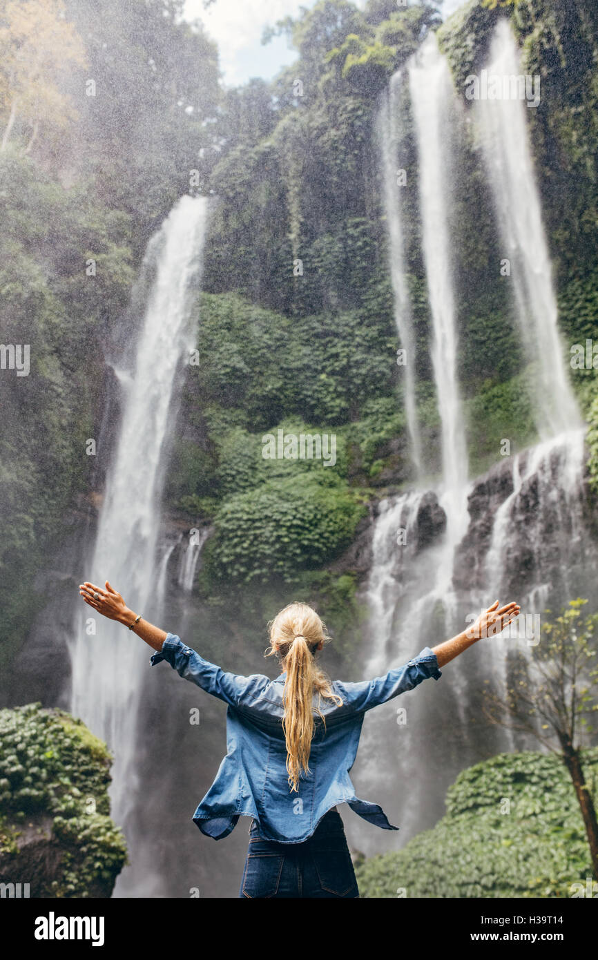 Vue arrière de la femme debout devant une chute d'eau avec ses mains posées. Touristiques femelle avec ses bras tendus à la recherche à w Banque D'Images