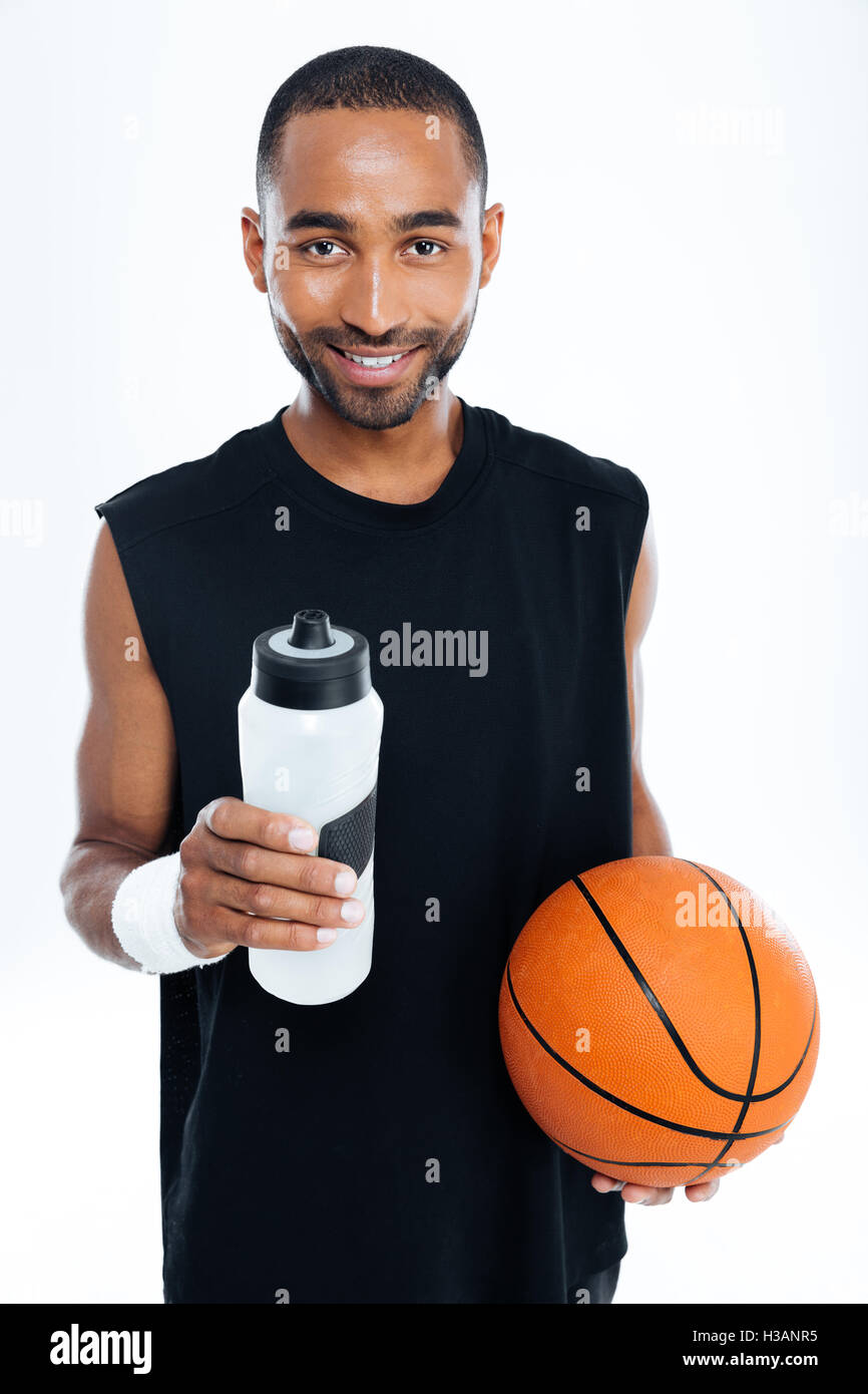 Portrait of a smiling young handsome sportsman holding basket ball et une bouteille d'eau isolé sur fond blanc Banque D'Images