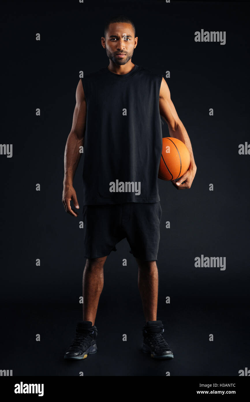 Concentrés african man holding sports Basket-ball et à la caméra à l'isolé sur un fond noir Banque D'Images