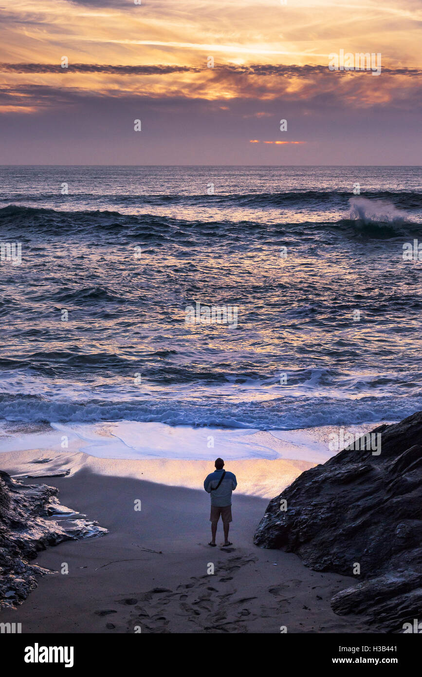 Un homme se tient sur la plage de Fistral peu au coucher du soleil. Banque D'Images