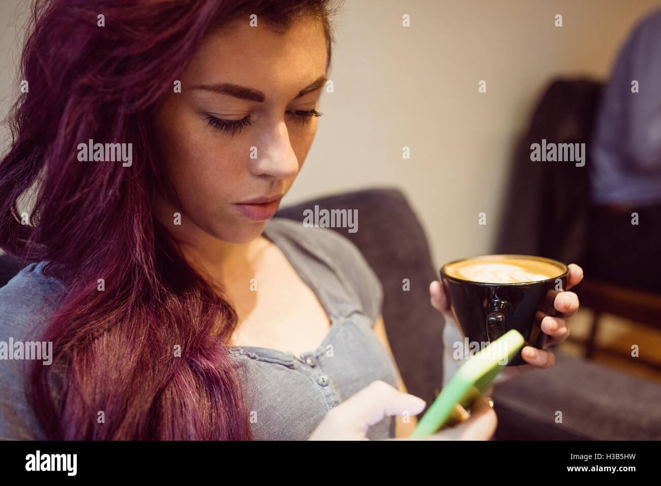 Femme de boire une tasse de café tout en utilisant un smartphone Banque D'Images