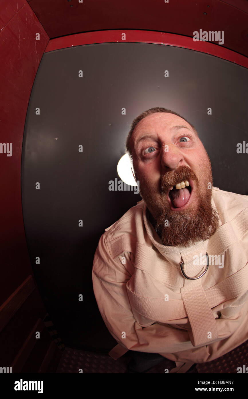 Photo d'un aliéné dans la quarantaine portant une camisole appuyé contre une porte de l'asile. Prises avec un objectif fisheye. Banque D'Images