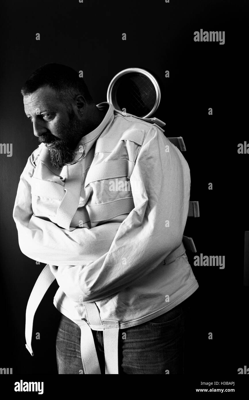 Photo d'un aliéné dans la quarantaine portant une camisole appuyé contre une porte de l'asile. Banque D'Images