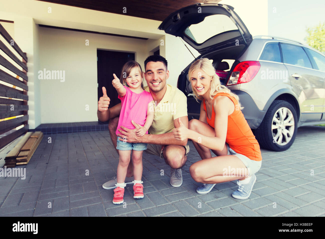 Famille heureuse avec showing Thumbs up voiture au parking Banque D'Images