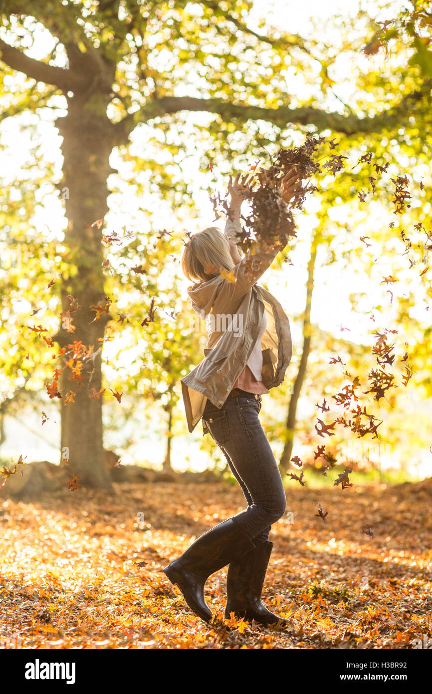 Woman throwing les feuilles d'automne en forêt sur sunny day Banque D'Images
