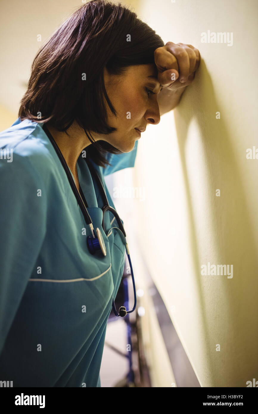 Infirmière déprimé leaning against wall Banque D'Images