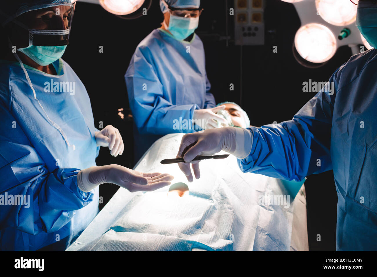 Opération donnant des chirurgiens à lame collègue en salle d'opération Banque D'Images