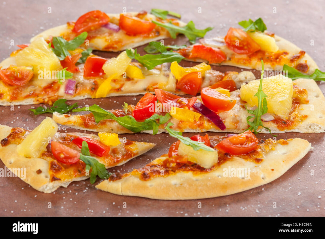 Pizza à croûte mince cuites sur pierre à l'ananas, le poivre et les oignons rouges saupoudré de sel de mer et de feuilles de roquette Banque D'Images
