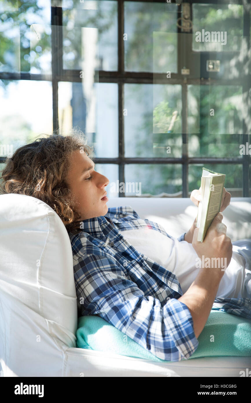 Young man reading book on couch Banque D'Images