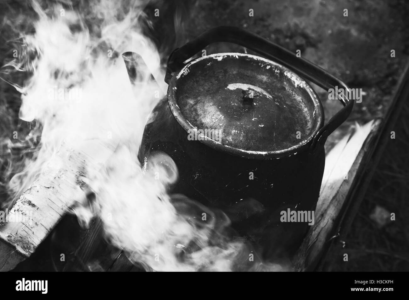 Vieille théière avec de l'eau bouillante se dresse sur un feu, noir et blanc Banque D'Images