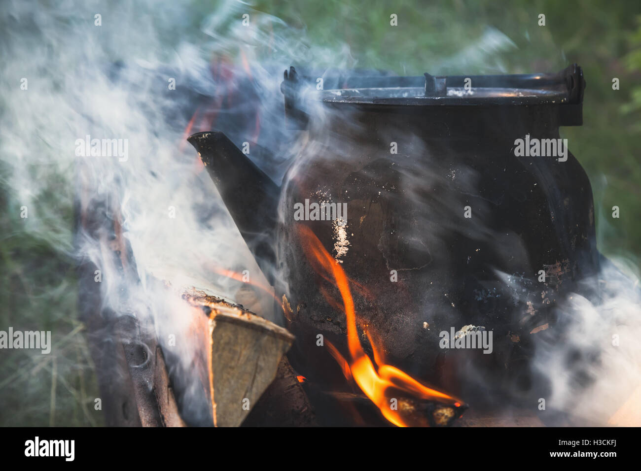 Ancienne théière noire avec de l'eau bouillante se dresse sur un feu de joie Banque D'Images