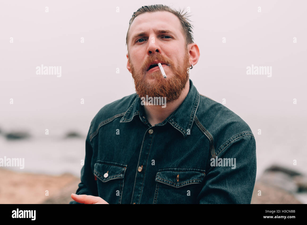 Homme barbu grave fumer une cigarette sur la plage Banque D'Images