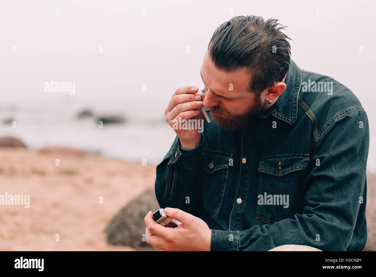 Homme barbu grave fumer une cigarette sur la plage Banque D'Images
