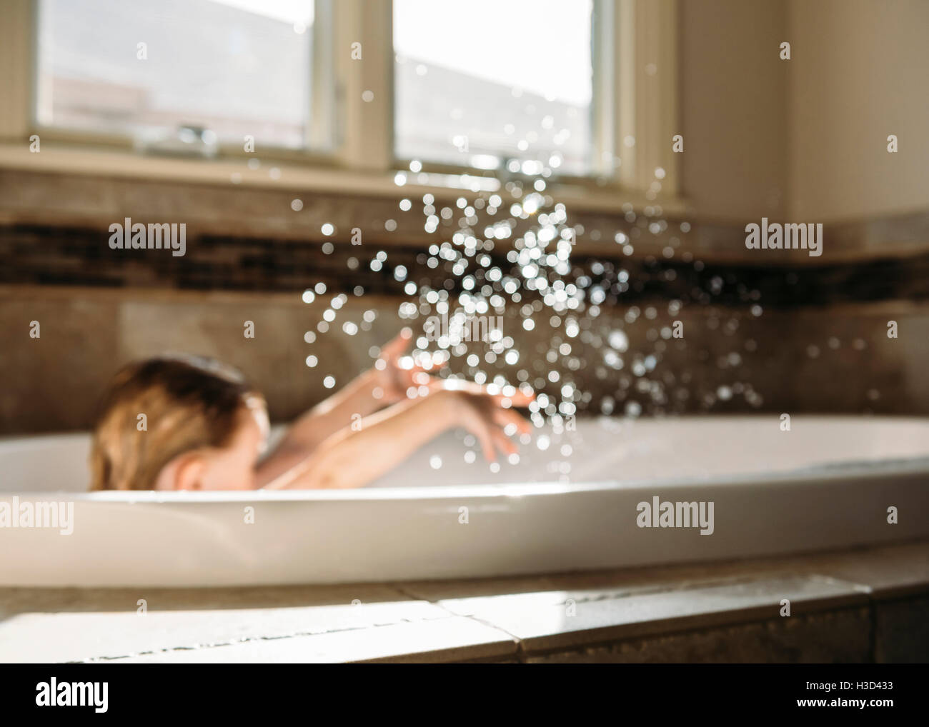 Garçon aux projections d'eau tout en restant assis dans une baignoire Banque D'Images