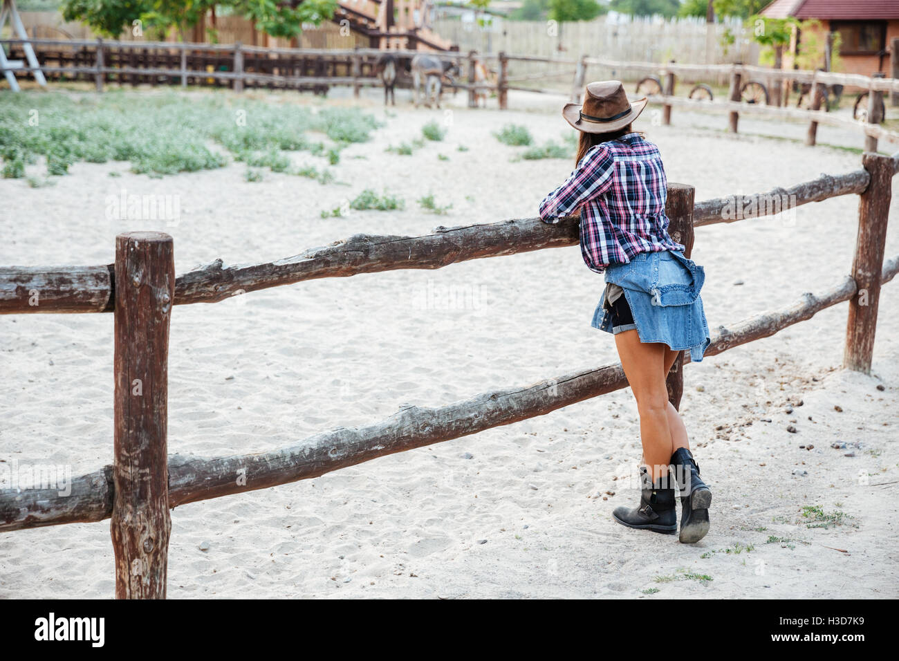Vue arrière de jeune femme au chapeau cowgirl debout près de clôture sur ranch Banque D'Images