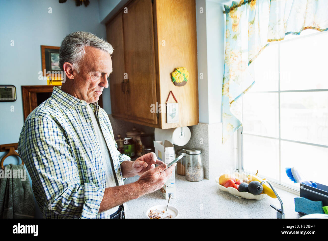 Man dans une cuisine, à l'aide d'un téléphone mobile. Banque D'Images