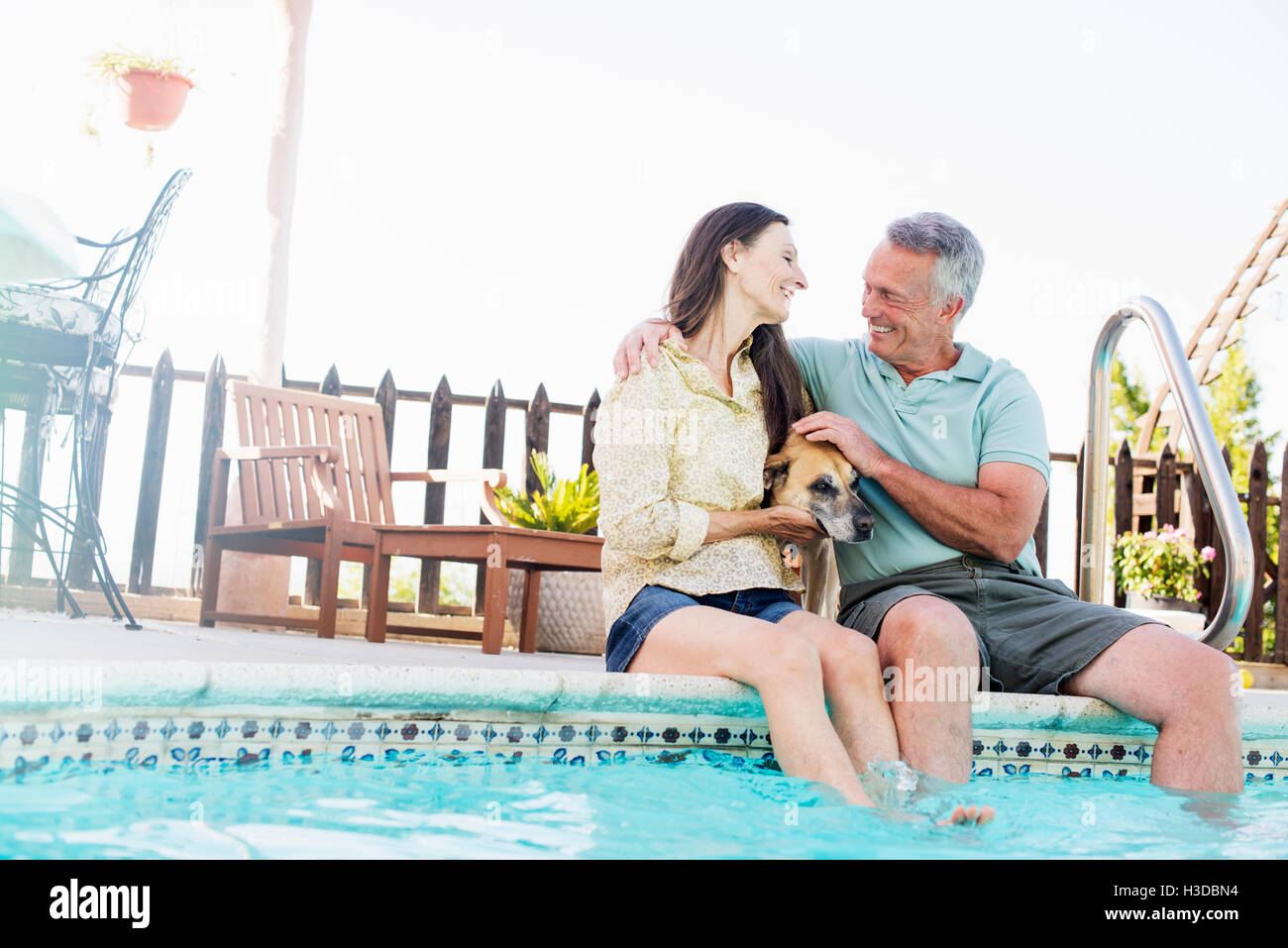 Un couple assis sur le bord d'une piscine, avec leur chien entre eux. Banque D'Images