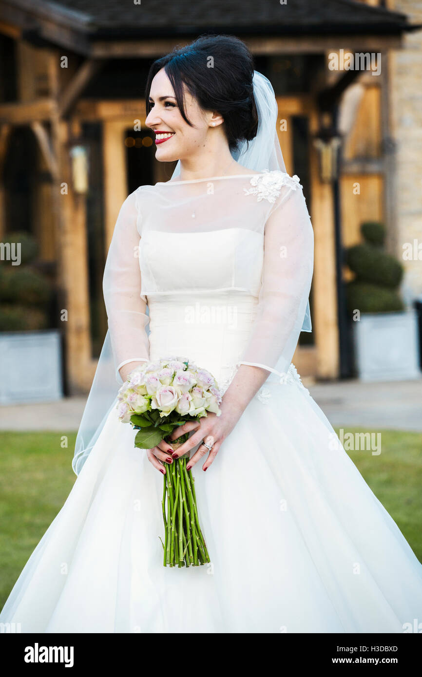 Une jeune mariée dans sa robe de mariage portant un bouquet. Banque D'Images