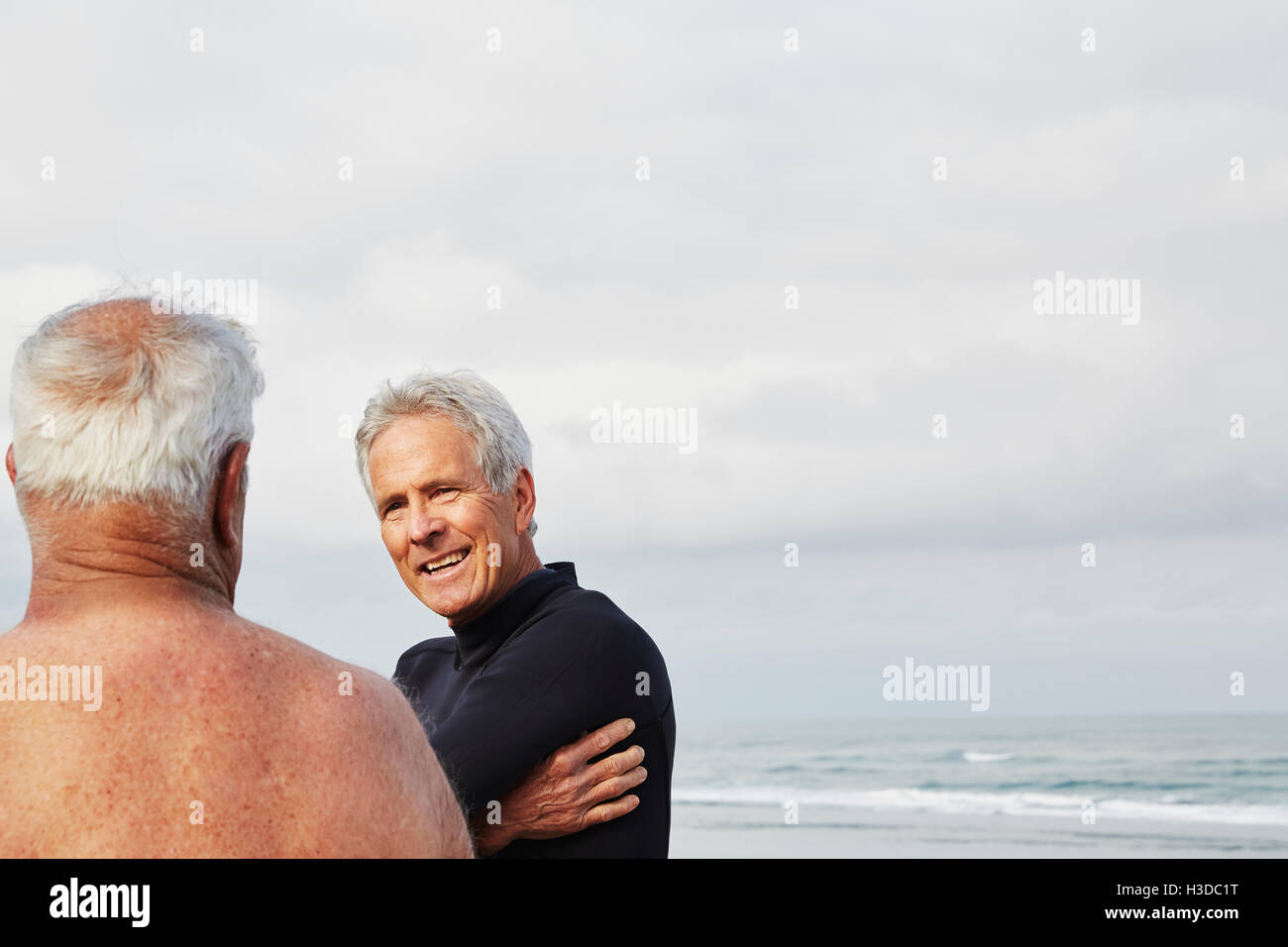 Deux hommes debout sur une plage, le chat, l'un de porter une combinaison isothermique. Banque D'Images