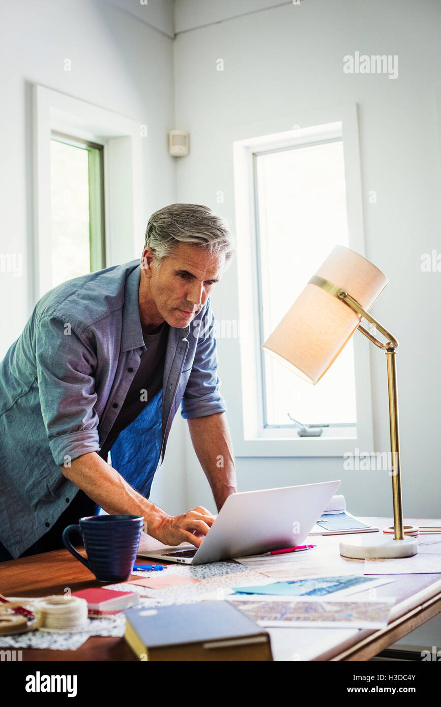 Un homme à la maison à l'aide d'un ordinateur portable sur un bureau. Banque D'Images
