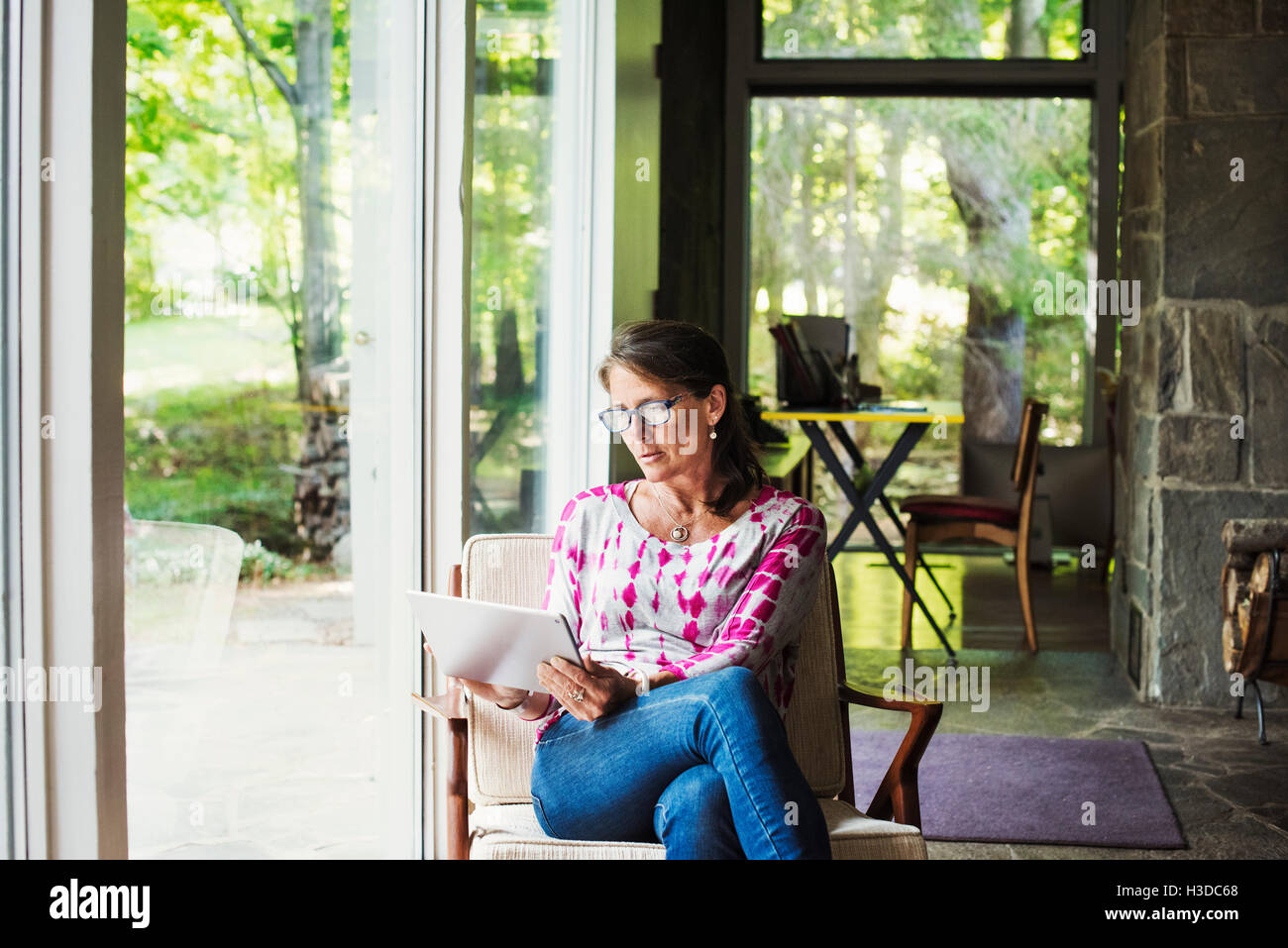 Une femme assise par une fenêtre avec une tablette numérique. Banque D'Images