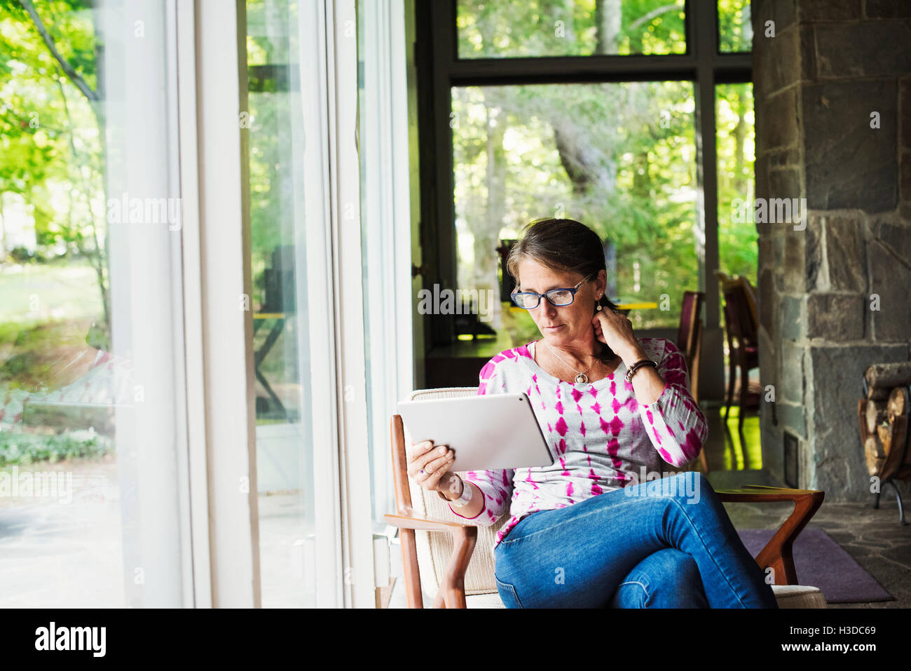Une femme assise par une fenêtre avec une tablette numérique. Banque D'Images