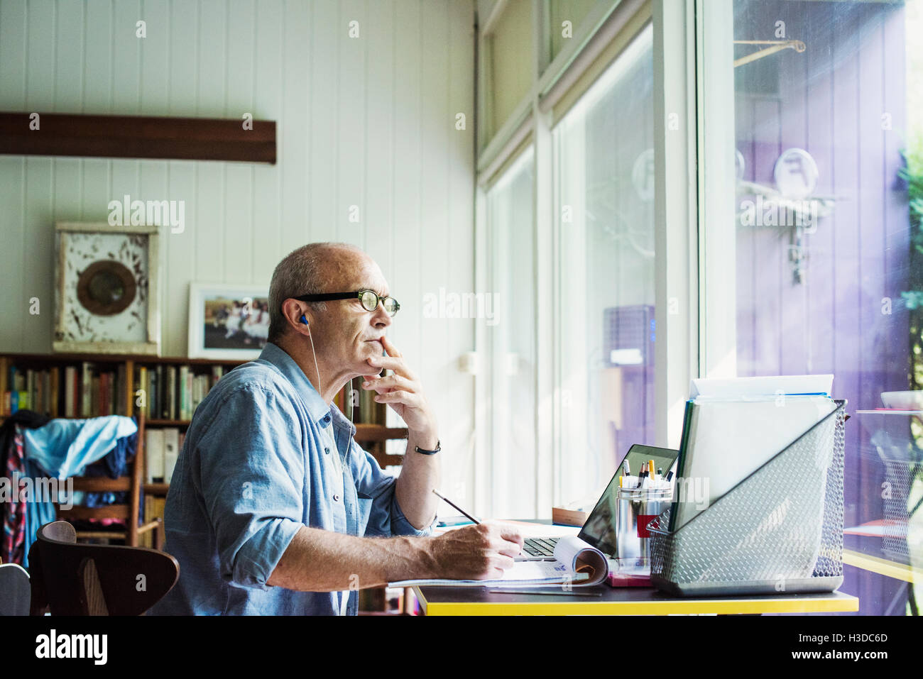 Un homme assis à un bureau à la maison, travailler sur un ordinateur portable. Banque D'Images