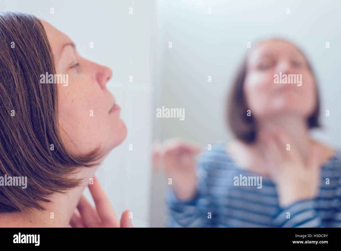 Jeune femme adulte, l'application de crème anti-vieillissement devant le miroir, selective focus Banque D'Images