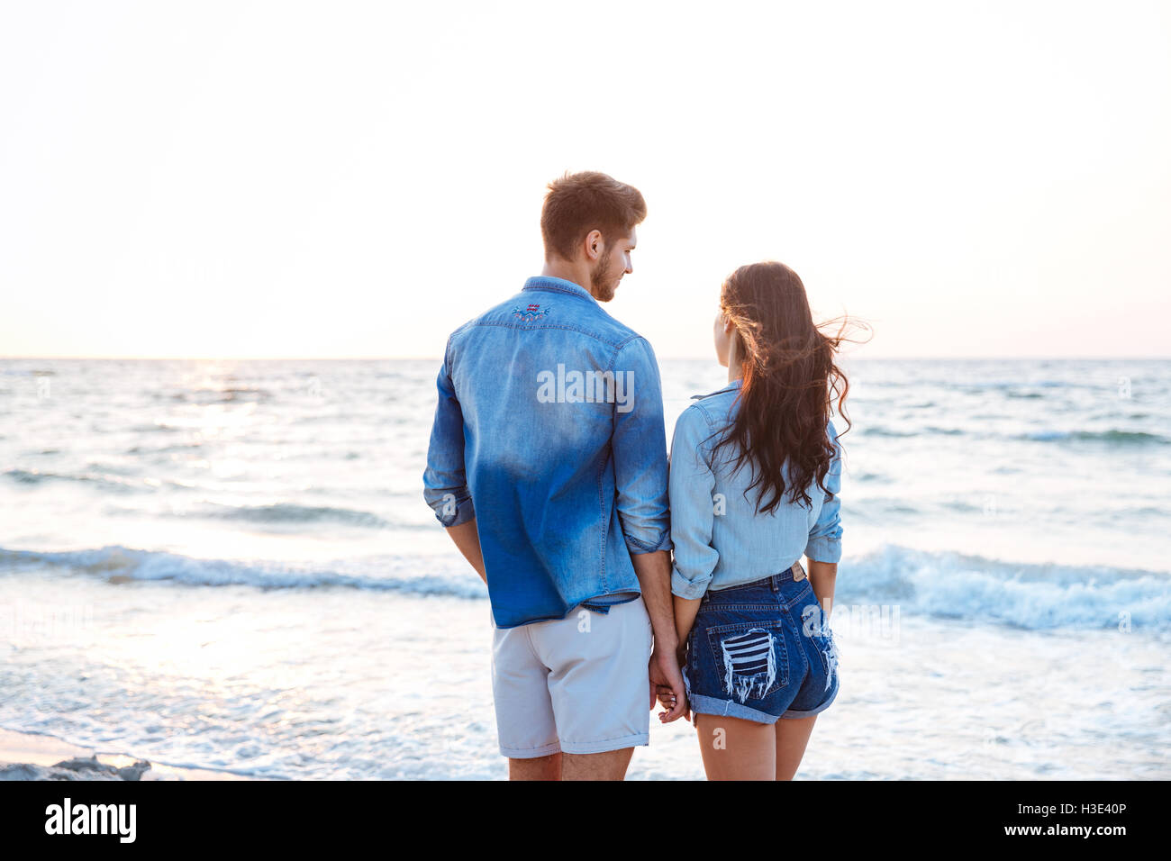 Vue arrière de l'heureux jeune couple debout et tenant les mains sur la plage Banque D'Images