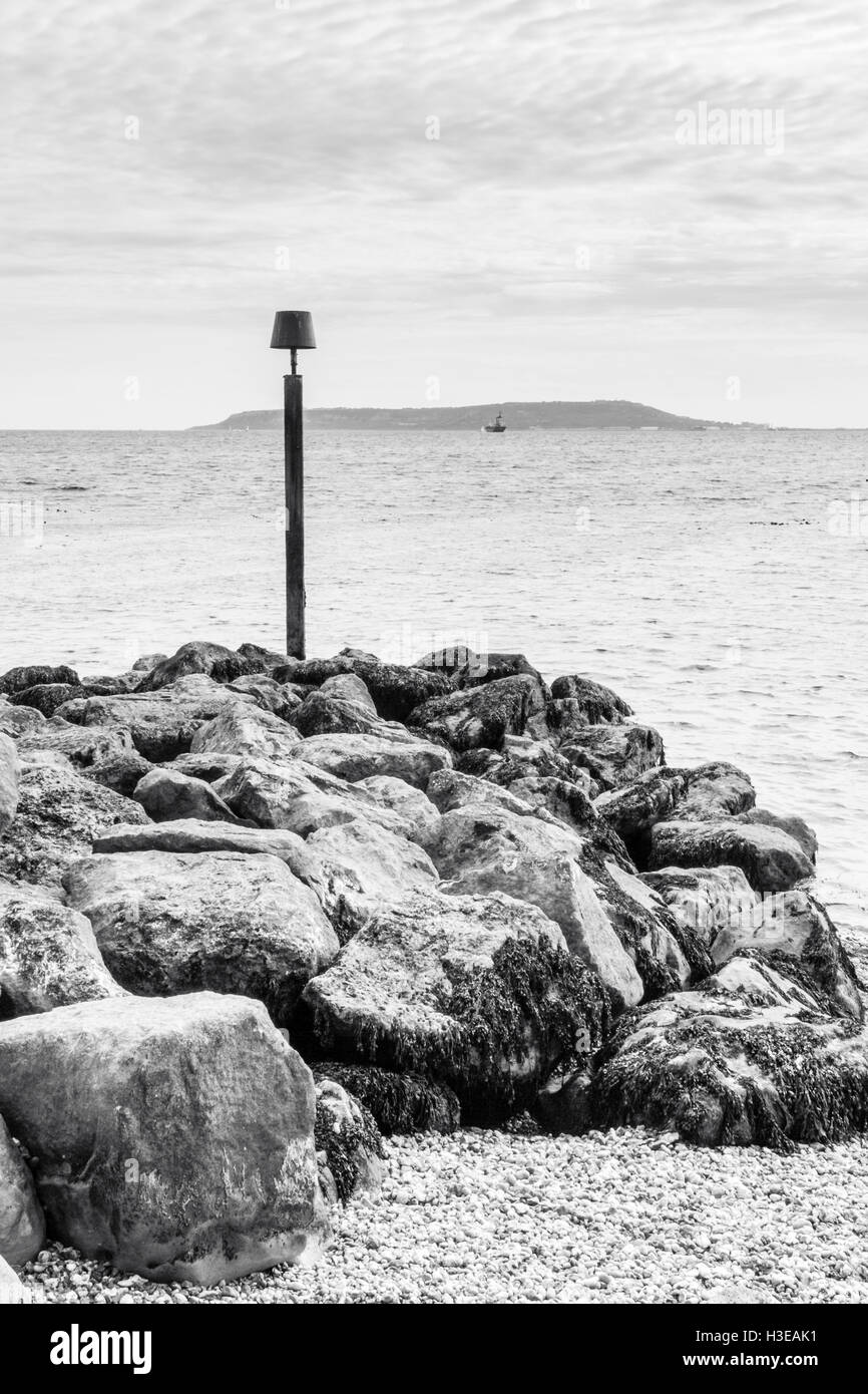 Image en noir et blanc d'un post d'avertissement sur un promontoire rocheux à Ringstead Bay, Dorset, England, UK, Portland Bill dans la distance Banque D'Images