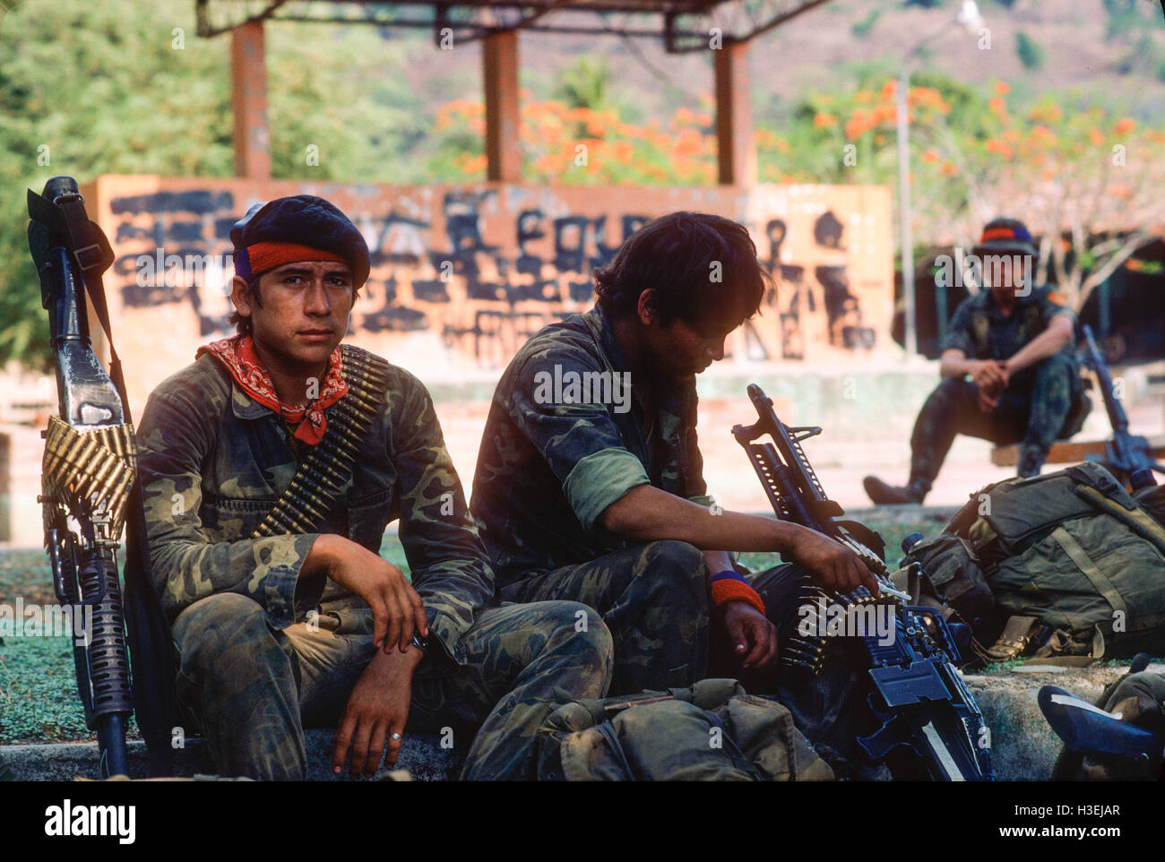 Trois soldats avec de l'équipement et des armes assis à l'extérieur, peut-être dans une jungle ou un cadre tropical. Banque D'Images