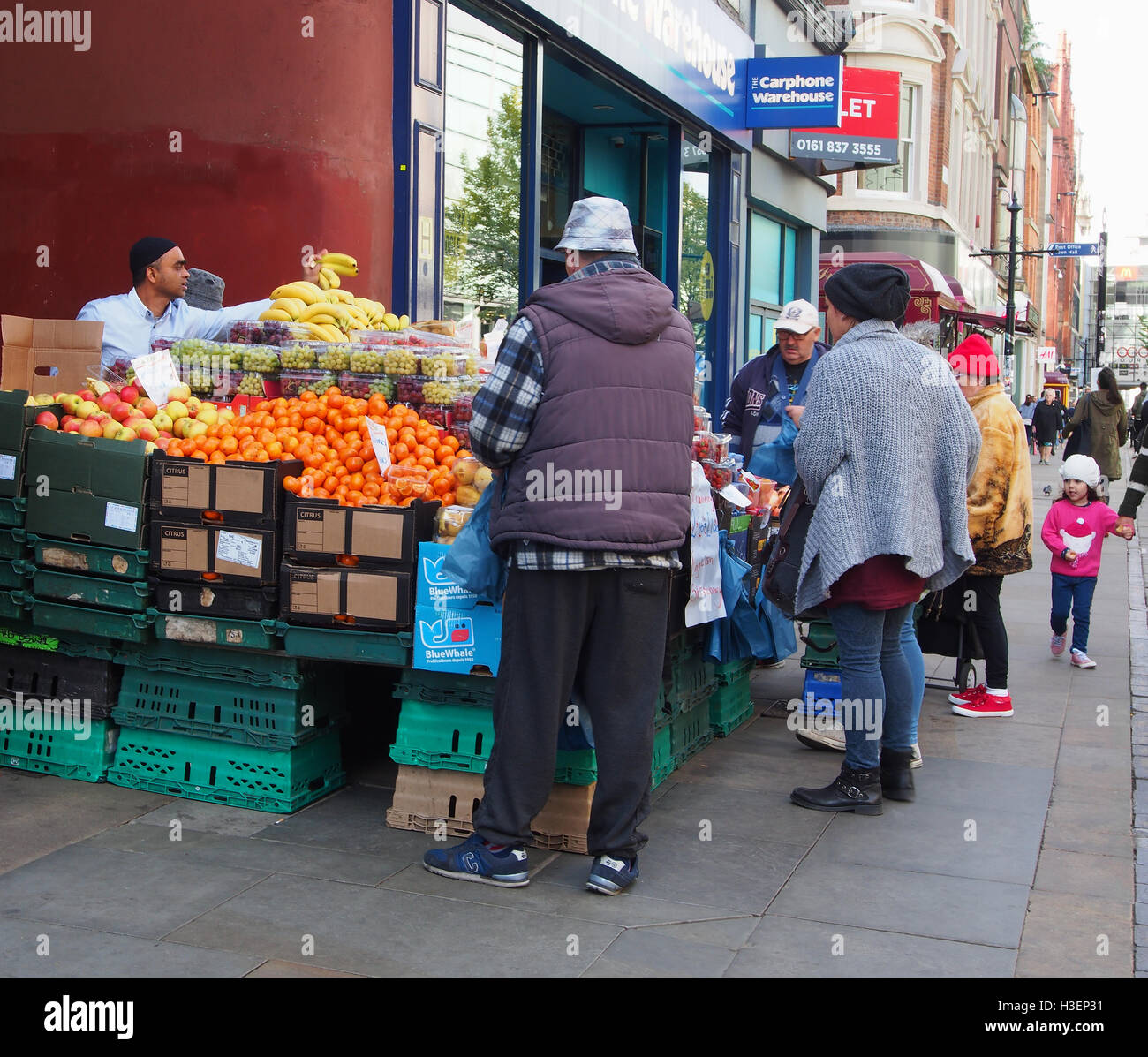 Décrochage du marché de fortune vendant des fruits sur la high street, dans le centre de Manchester, avec de nombreux clients intéressés et le vendeur servant les bananes. Banque D'Images
