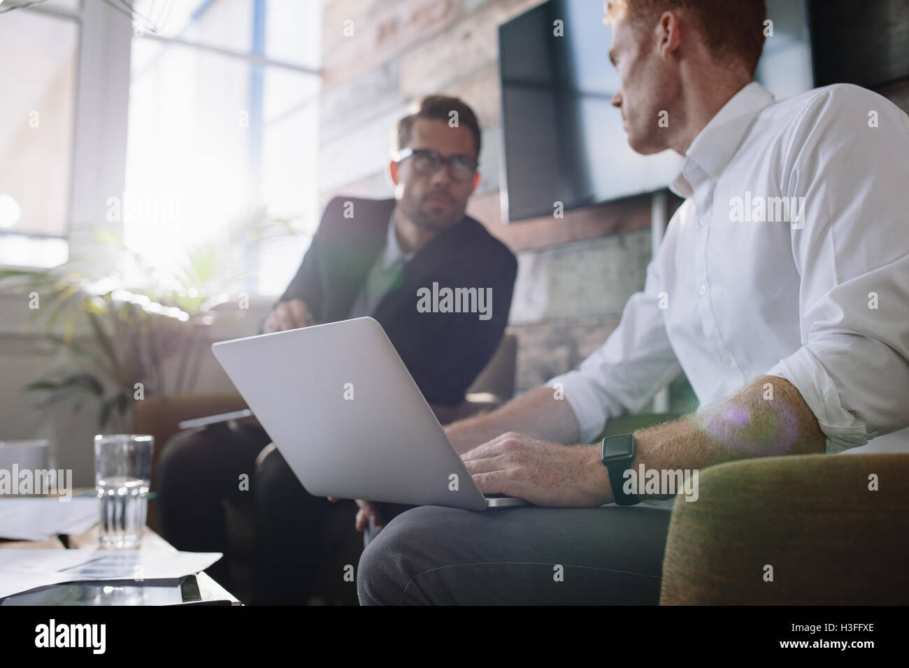 Deux jeune homme assis dans le bureau et discuter affaires. Businessman with laptop parler avec tes collègues au cours de réunion. Banque D'Images