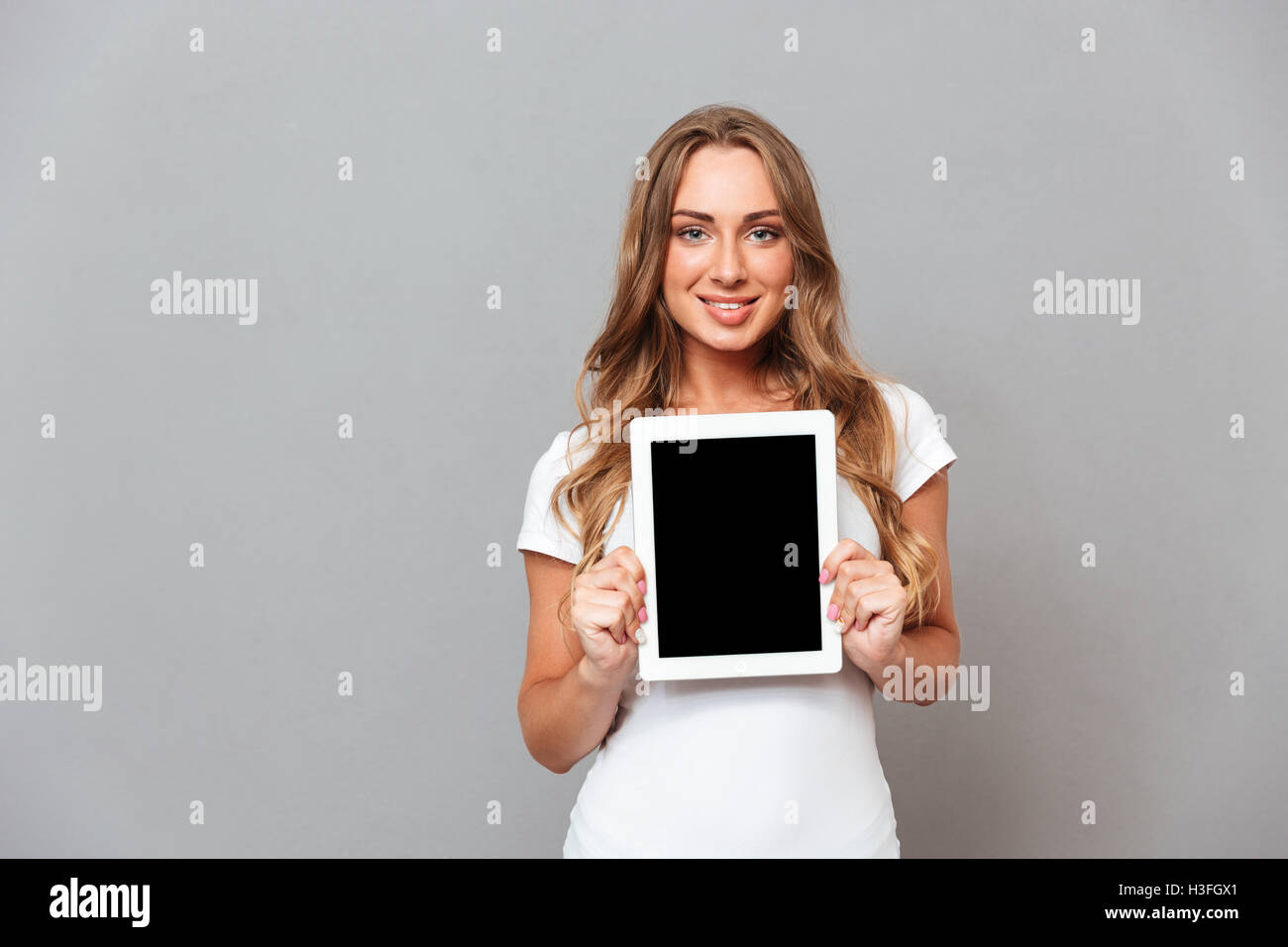 Belle jeune femme montrant l'ordinateur tablette avec écran blanc isolé sur fond gris Banque D'Images