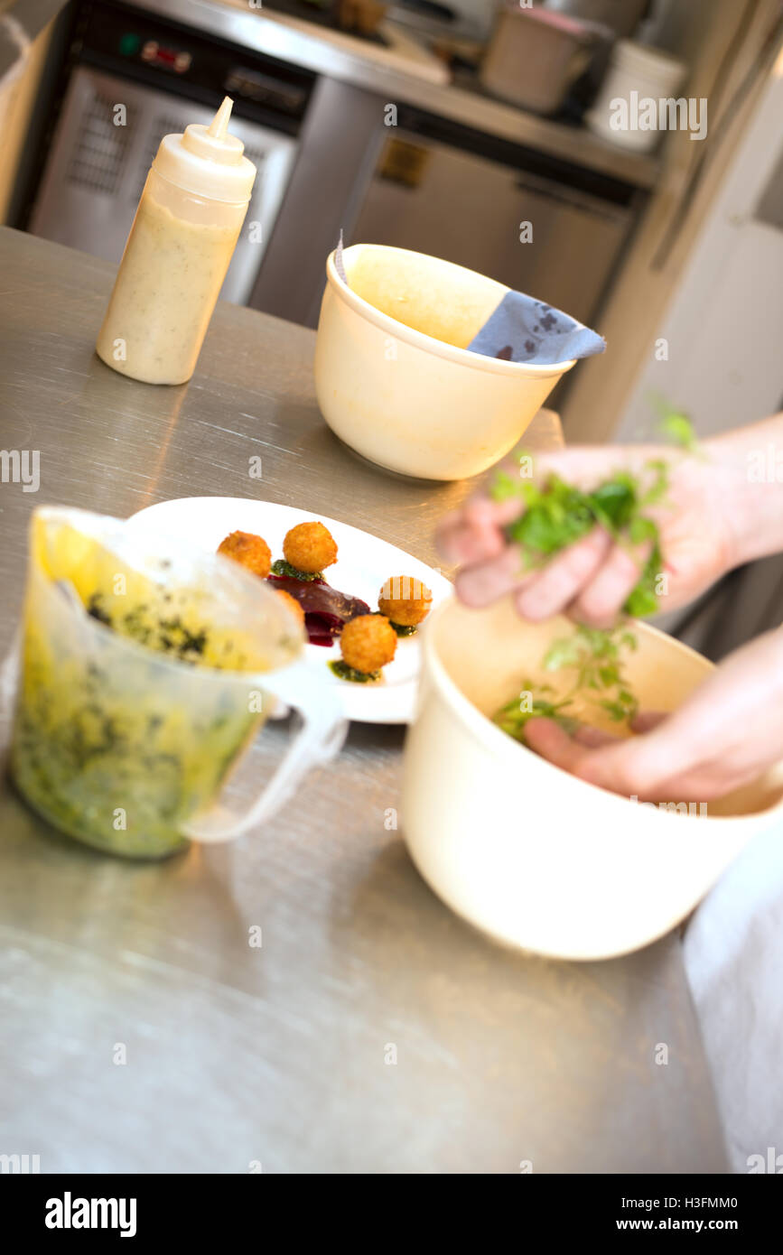 Mains jetant la salade dans un bol à l'intérieur d'une cuisine Banque D'Images