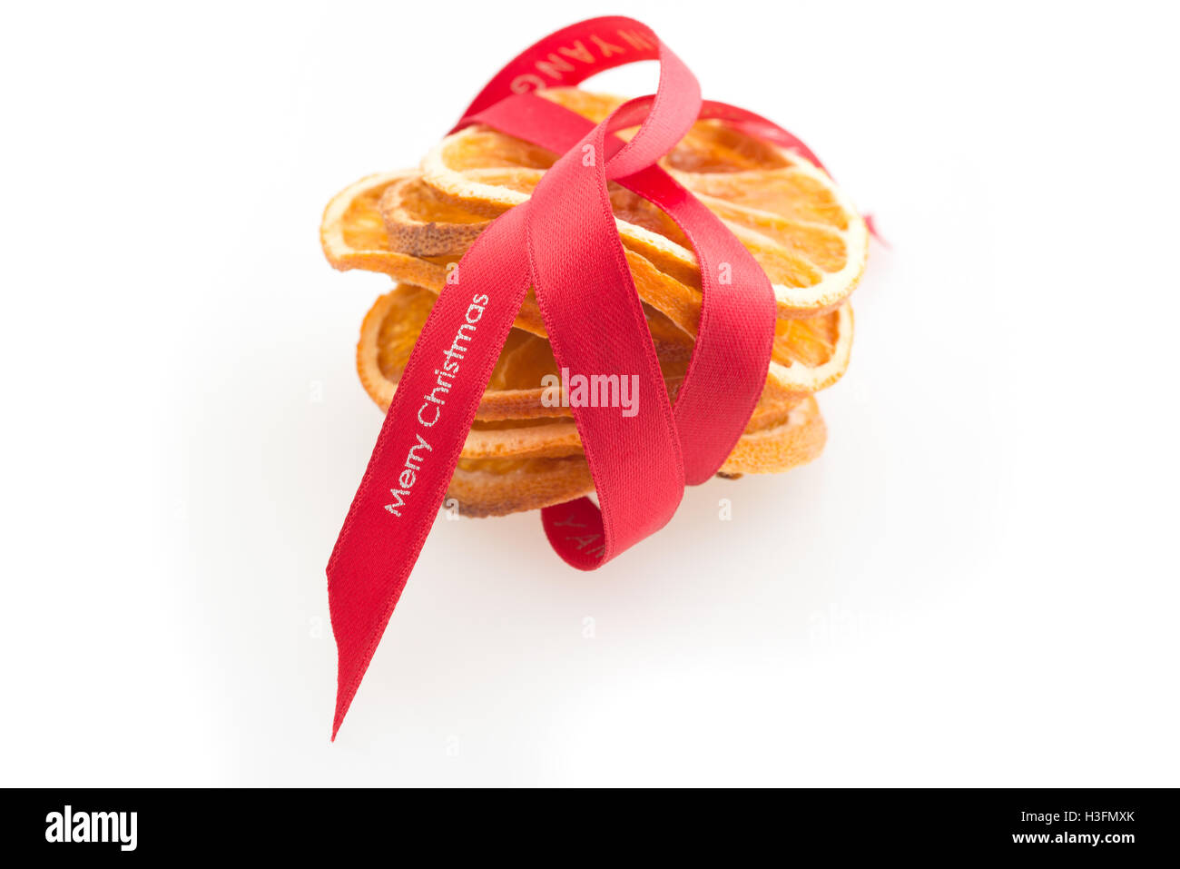 Décoration d'un empilement de tranches de fruits orange séchées décoratives attachées avec un rouge "Joyeux Noël" ruban. Banque D'Images