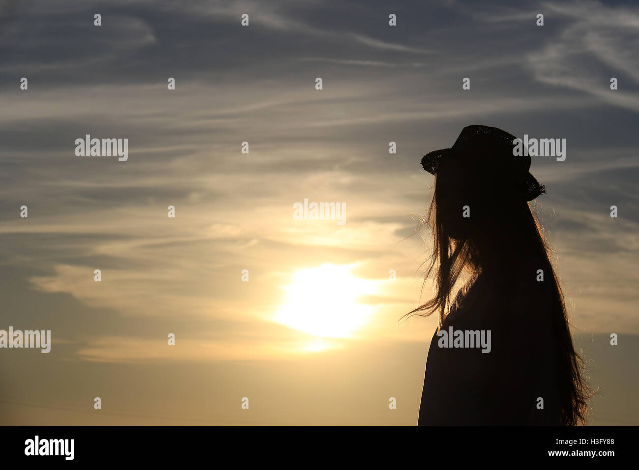 La silhouette d'une fille contre le soleil avec des cheveux d'or, elle porte un chapeau. Banque D'Images