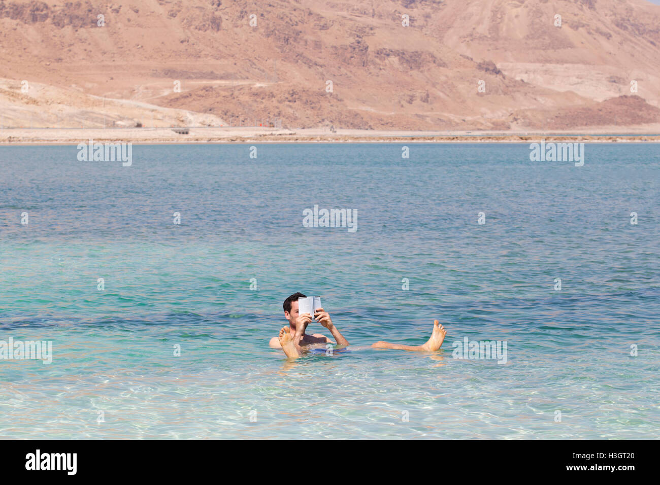 Un touriste lisant un livre en se baignant dans le lac salé de la mer Morte. Ein Bokek, Israël. Banque D'Images
