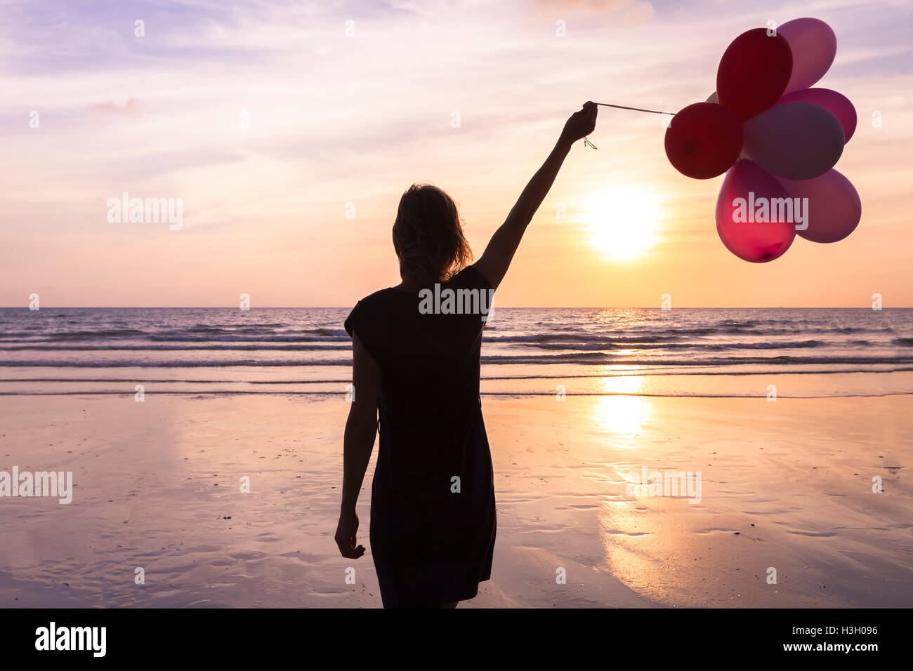 Jeune femme avec des ballons d'hélium dans la main marcher sur la plage au coucher du soleil, concept à propos anniversaire et des événements heureux Banque D'Images