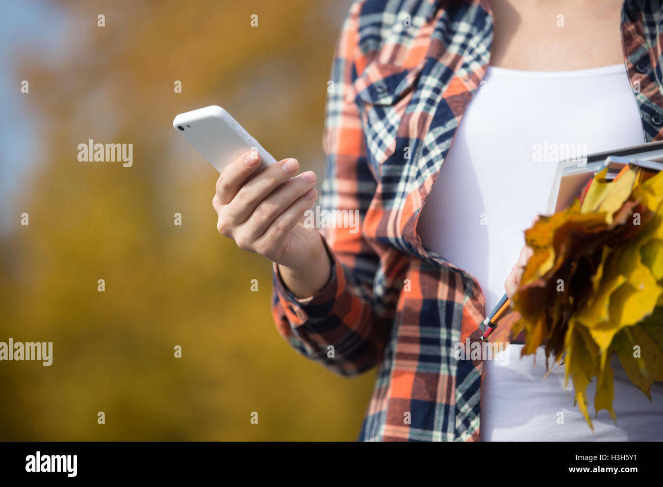 Femme holding phone dans la main, des feuilles jaunes dans un autre Banque D'Images