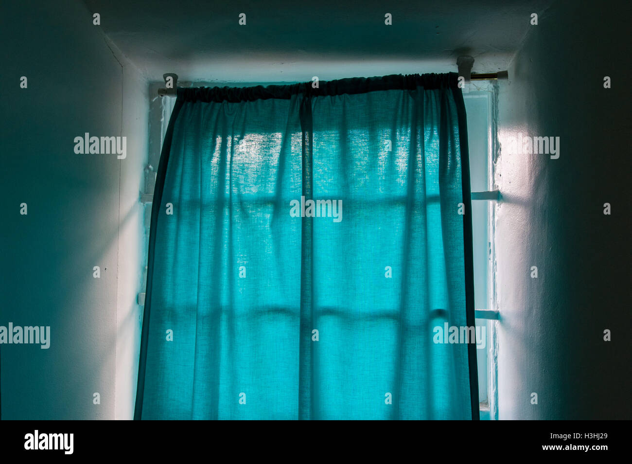 Rideaux turquoise lumineux dans une fenêtre ensoleillée adobe blanc Banque D'Images