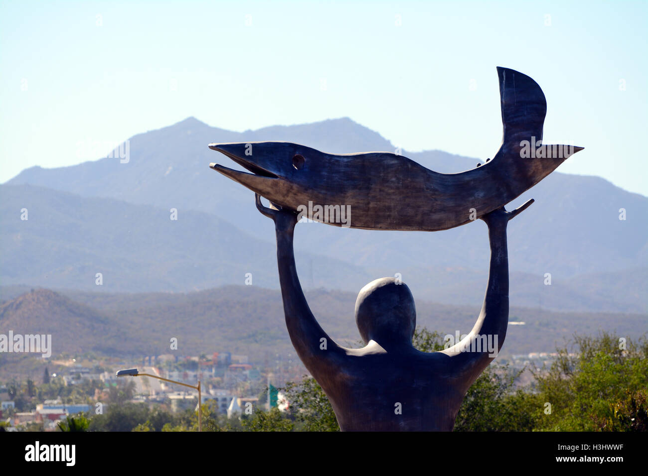 Close-Up Statue d'un homme tenant un poisson vers le soleil Ciel au Jardin botanique de Wirikuta, le Mexique avec des montagnes et ciel bleu Banque D'Images